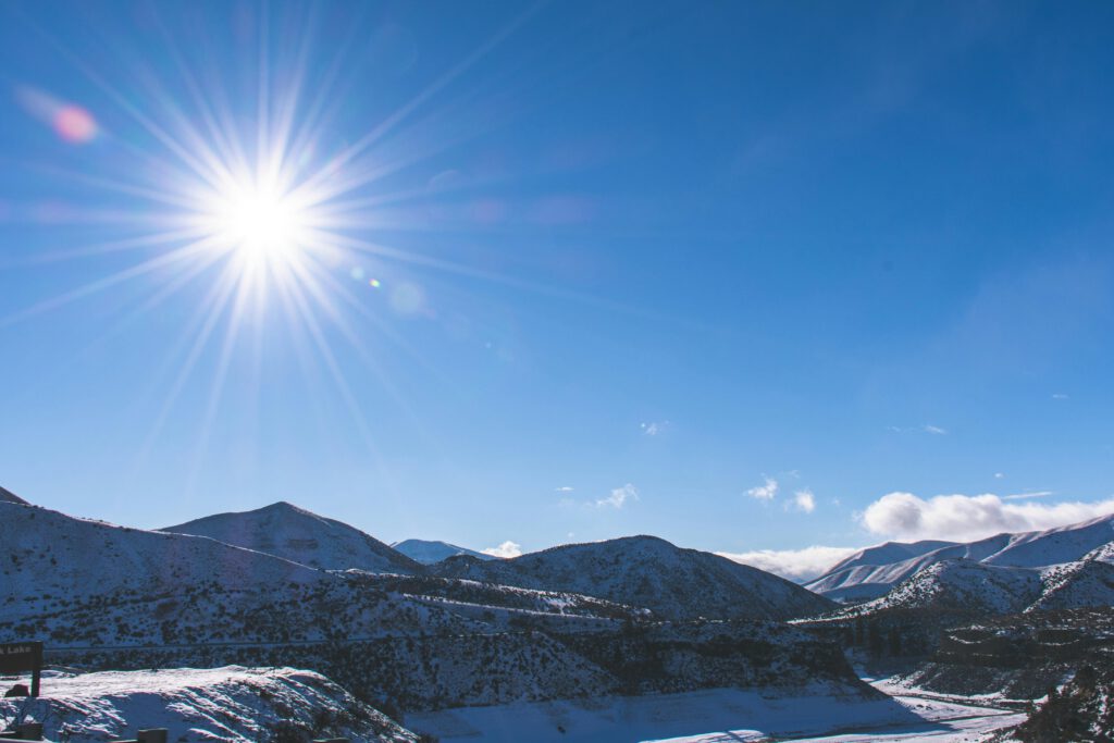 A stunning winter mountain landscape with a bright sun and clear blue sky.